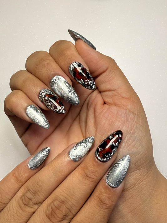 Hand with chrome silver cat eye tortoise shell nail set and black nail art on a plain background