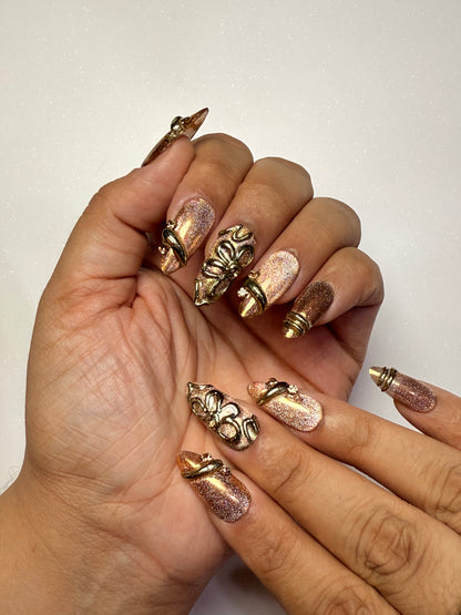 Hand with intricately designed nails featuring gold and bronze elements on a plain background brown cat eye press on nail set  3D nail set chrome nail set