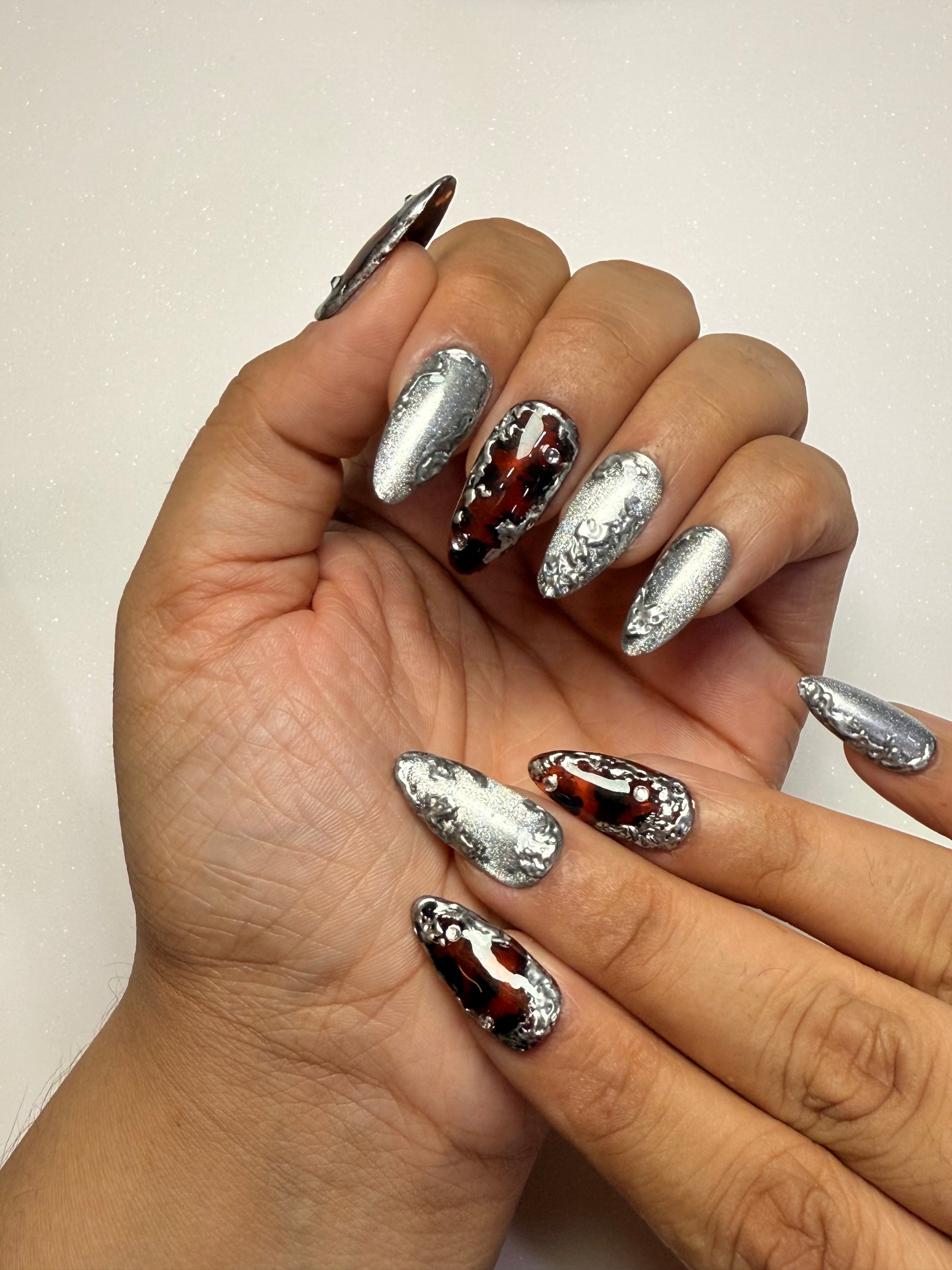 Hand with metallic nail art chrome silver cat eye tortoise shell nail set on a plain background