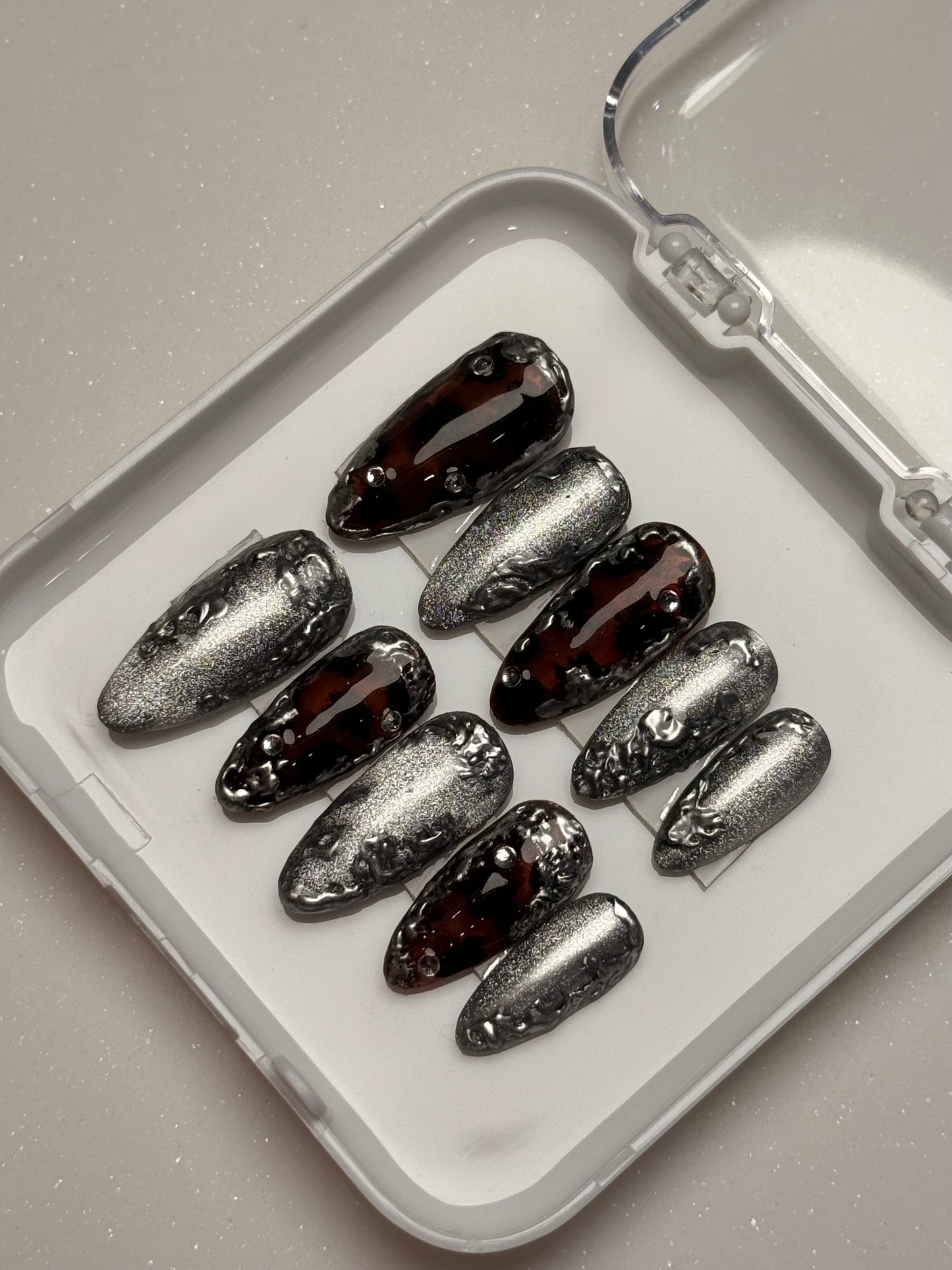 Set of silver cat eye, tortoise shell nails and black stiletto nails in a clear case on a light gray background