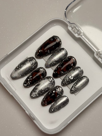 Set of silver cat eye, tortoise shell nails and black stiletto nails in a clear case on a light gray background
