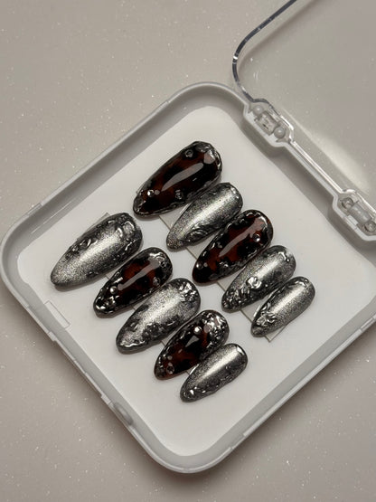 Set of silver cat eye and dark brown nail art tortoise shell nail set components on a white tray with a clear lid.