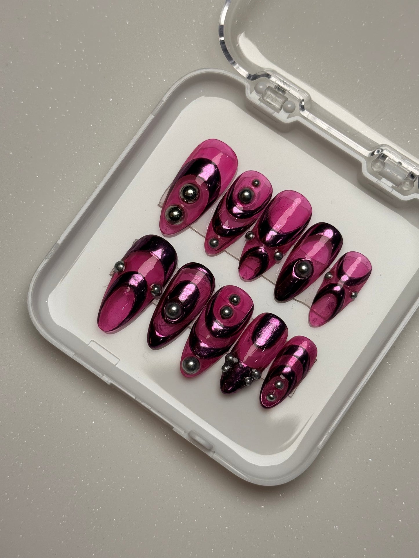 Set of purple nail art designs in a clear case on a gray background pink chrome nail set abstract nail set 