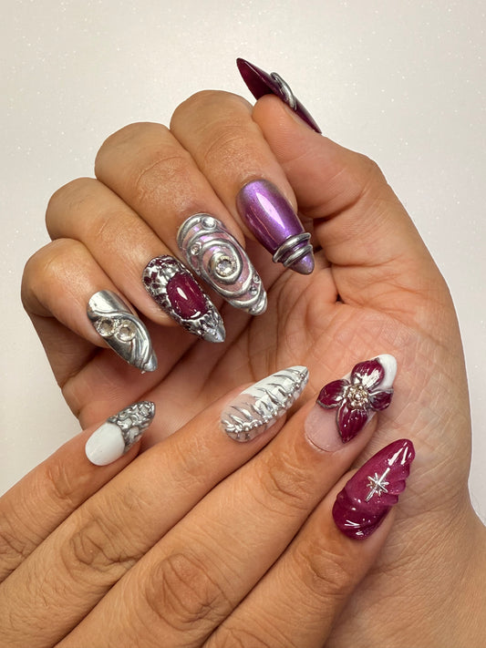 Hand with decorative nails featuring purple, silver, and white designs on a plain background chrome nail set 3D flower nail set  purple nail set