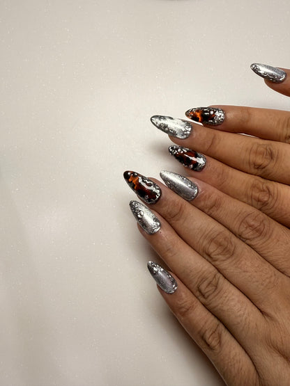 Close-up of hands with silver cat eye, chrome, tortoise shell and black nail art on a light background