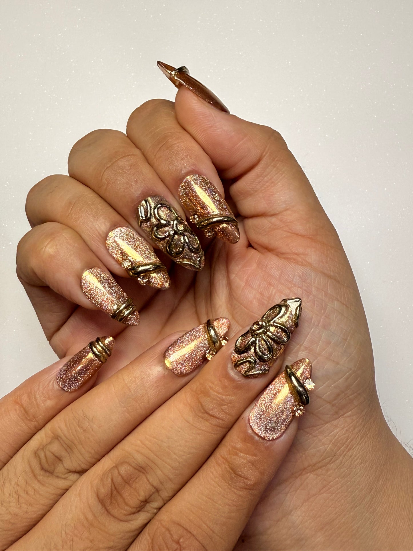 Hand with decorative nail art featuring gold and rose gold designs on a neutral background brown cat eye press on nail set  3D nail set chrome nail set