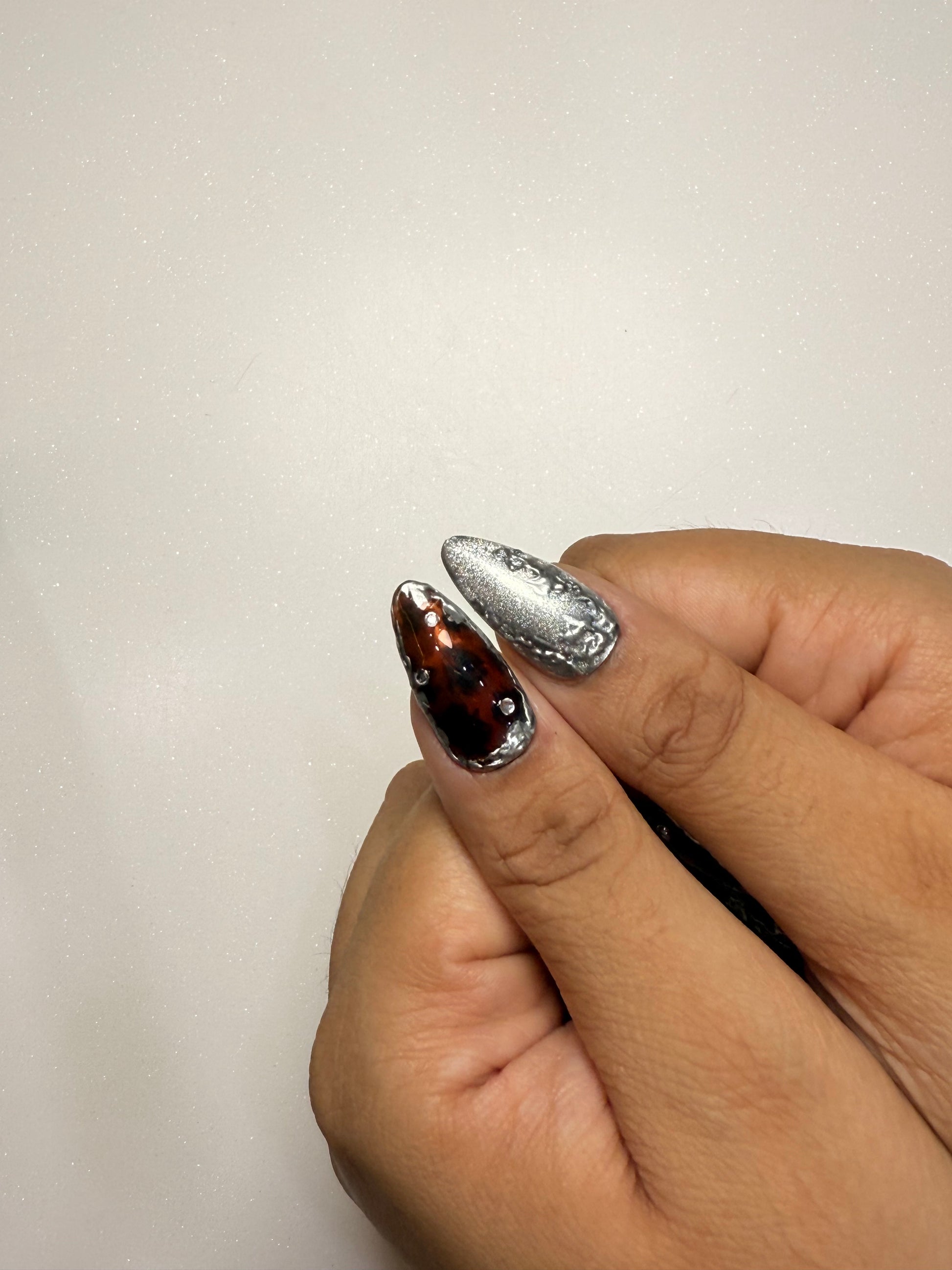 Close-up of a hand with silver cat eye tortoise shell and black nail art on a plain background
