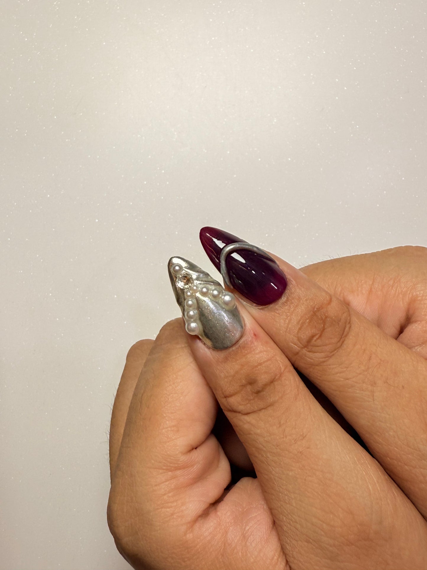 Hand wearing a silver ring with a pearl design on a plain background chrome nail set 3D flower nail set  purple nail set