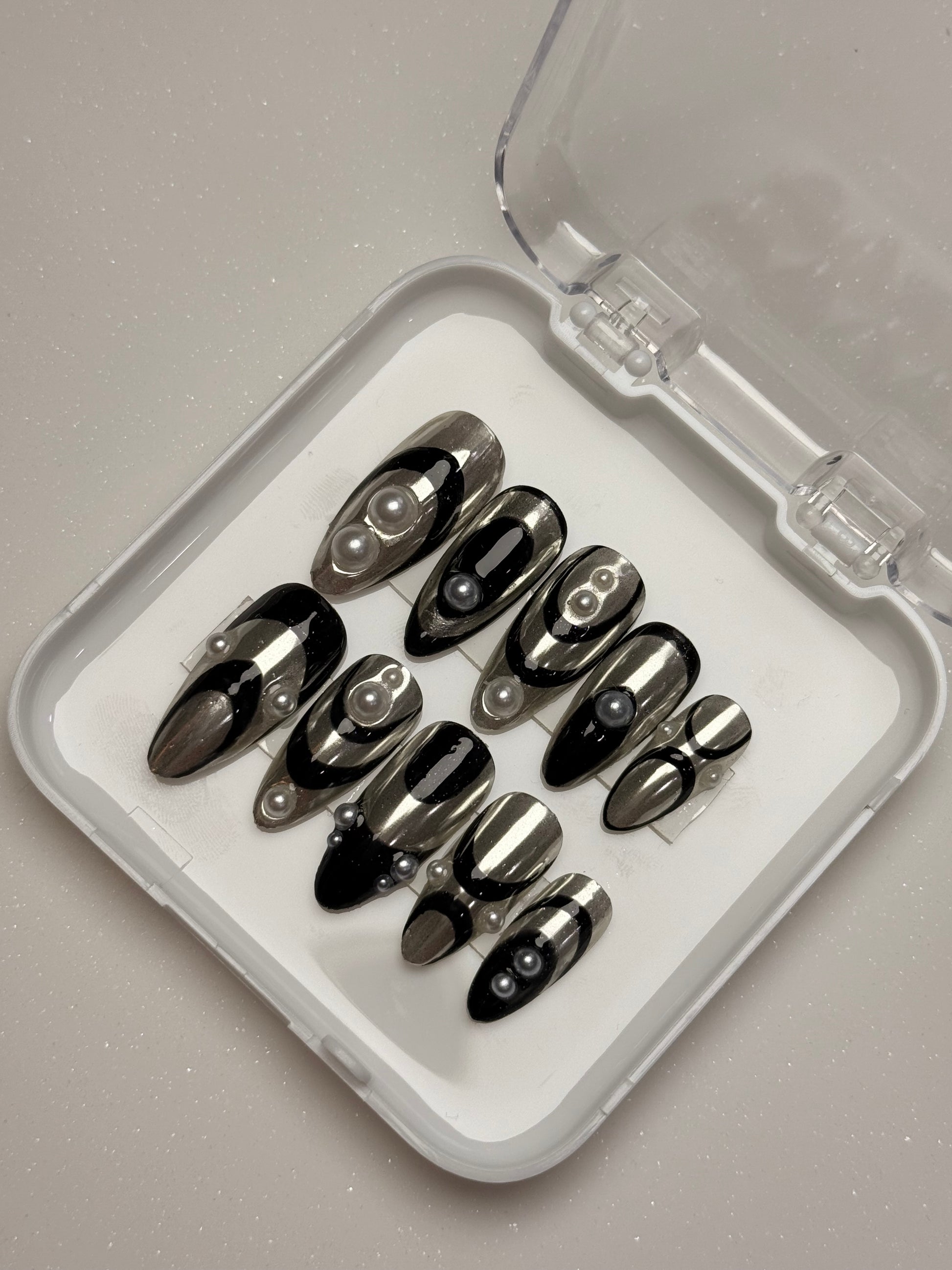 Set of black stiletto nails in a clear case on a gray background silver chrome nail set abstract nail set 