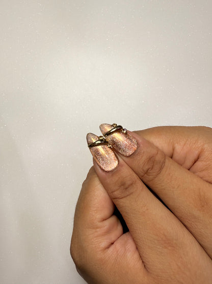 Hand with pink glittery nail polish holding a small object on a light background brown cat eye press on nail set  3D nail set chrome nail set