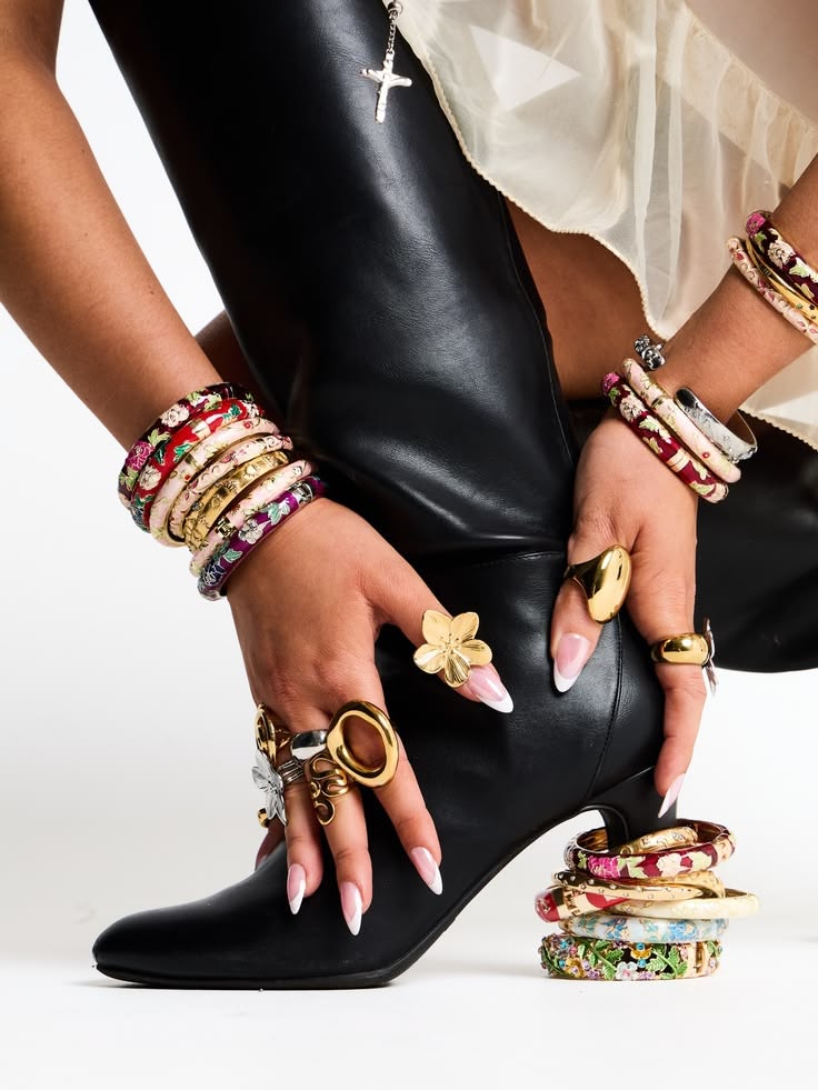 Soft pink French-tip almond press-on nails with a gold flower ring and floral cloisonné bangles resting on a black leather boot