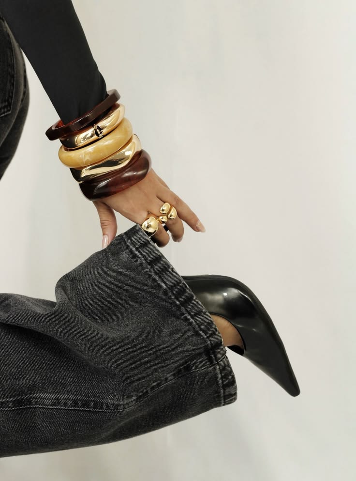 Chunky gold, cream and tortoiseshell bangles stacked above a bare manicure, styled with washed denim and a black stiletto heel