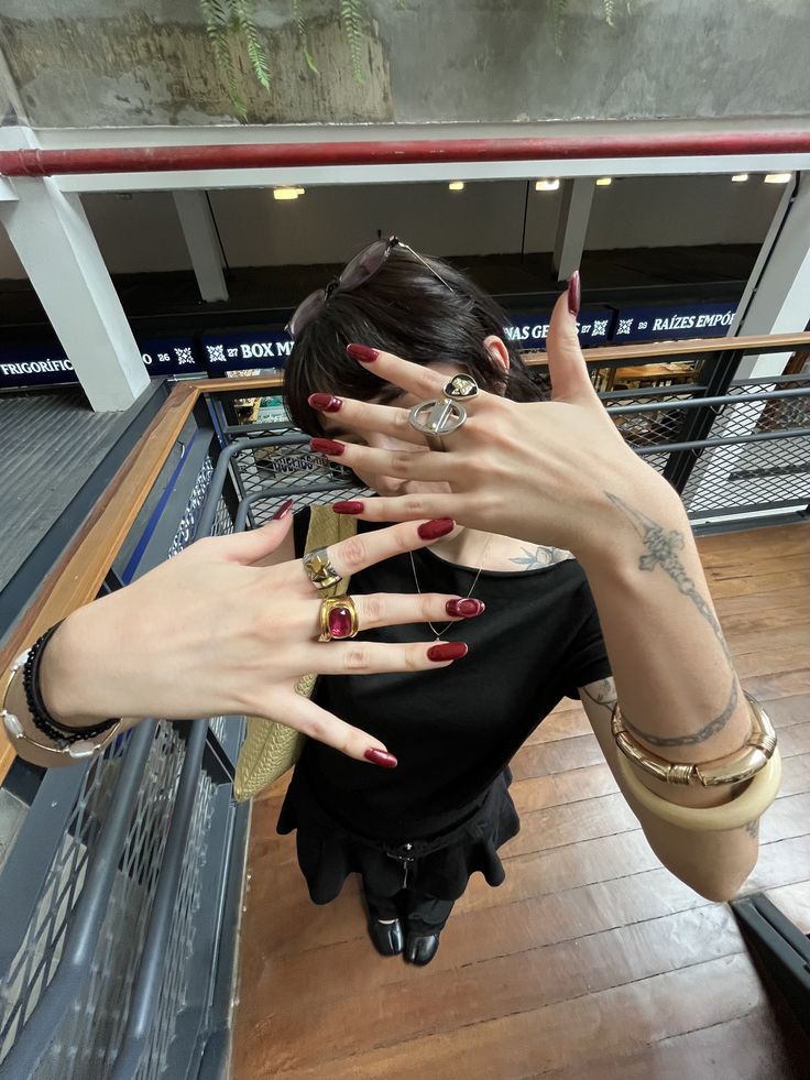 Deep wine-red press-on nails fanned across the face, layered with bold gold rings, bracelets and a bangle. Party-ready evening look